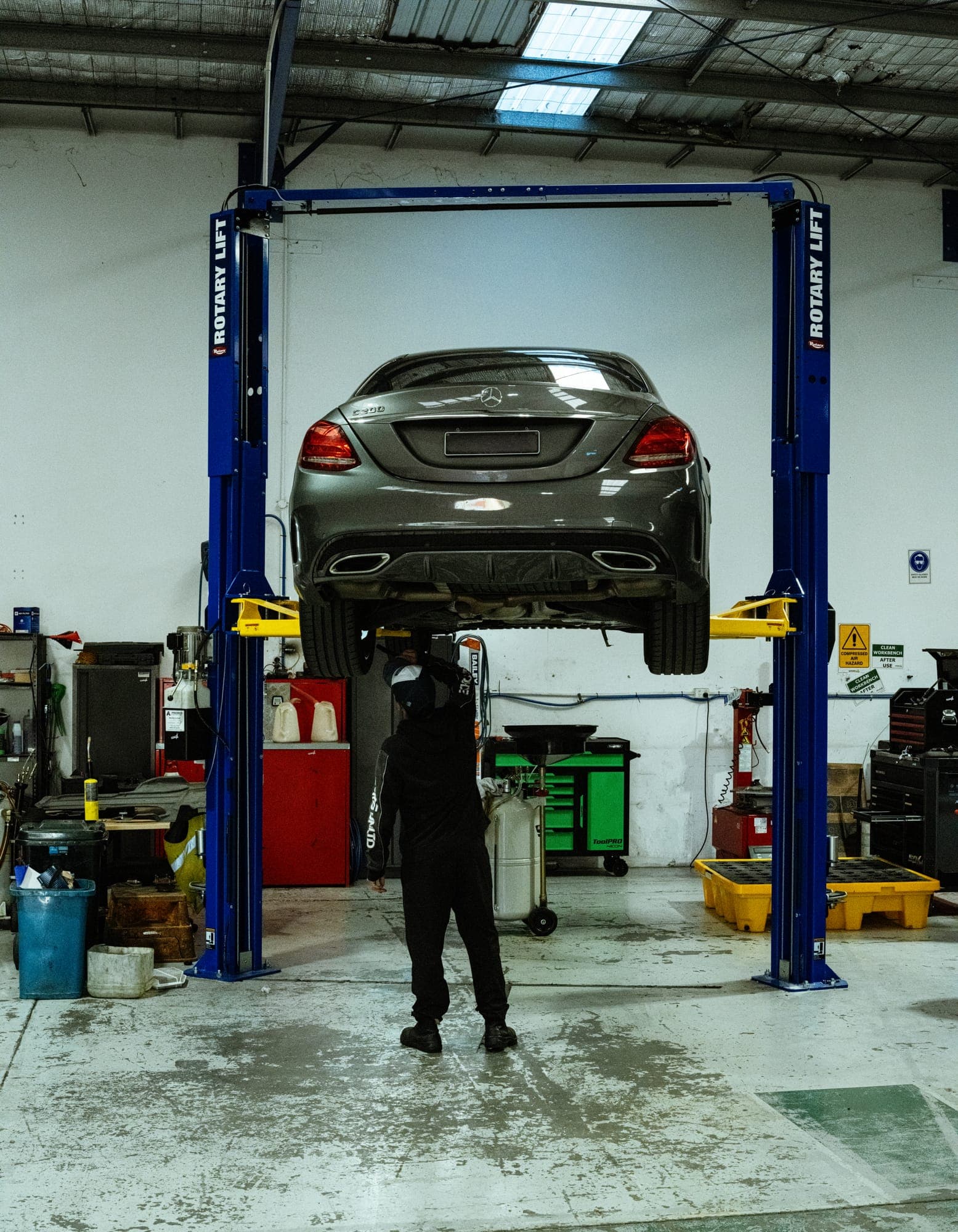 A Mercedes-Benz C200 raised on the two-post hoist with a technician working underneath