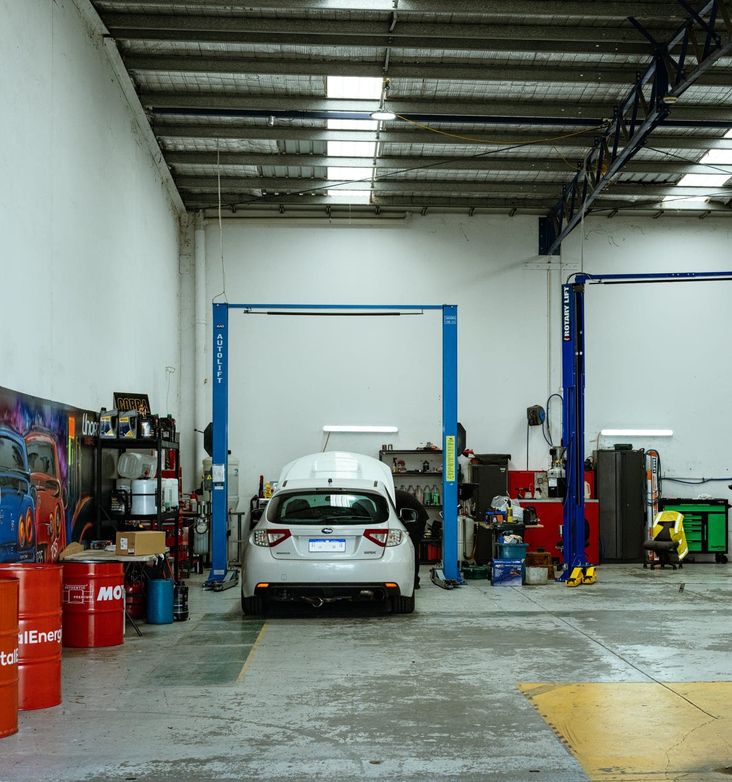 Looking into the Unorthodox Automotive workshop from the entrance, with both hoists and a Subaru WRX on the floor